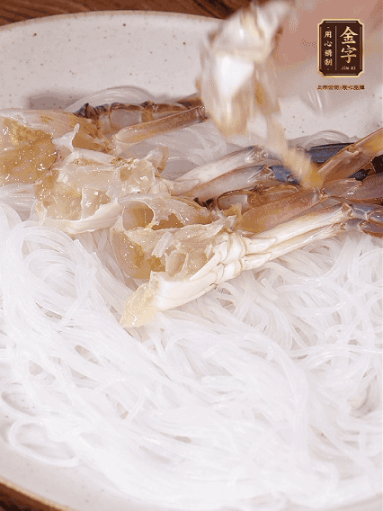 盤底墊上粉絲，擺上梭子蟹、火腿片，撒姜粒，淋上蒸魚豉油、花雕酒調(diào)味腌制15分鐘